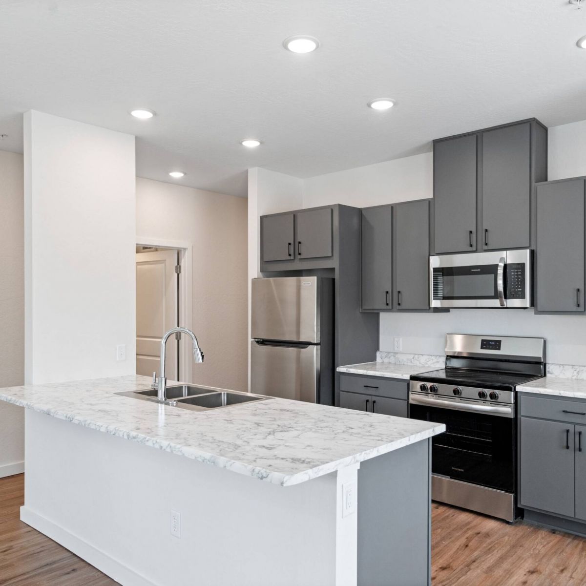 Sierra on 66 Modern kitchen with gray cabinets, stainless steel appliances, and a marble island countertop.