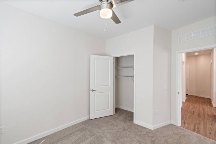 Sierra on 66 Empty room with beige carpet, white walls, open closet, ceiling fan, and a view into a hallway.
