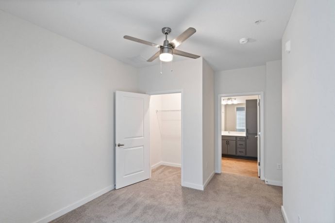 Sierra on 66 Empty bedroom with beige carpet, ceiling fan, open closet door, and view into a bathroom with double sinks.