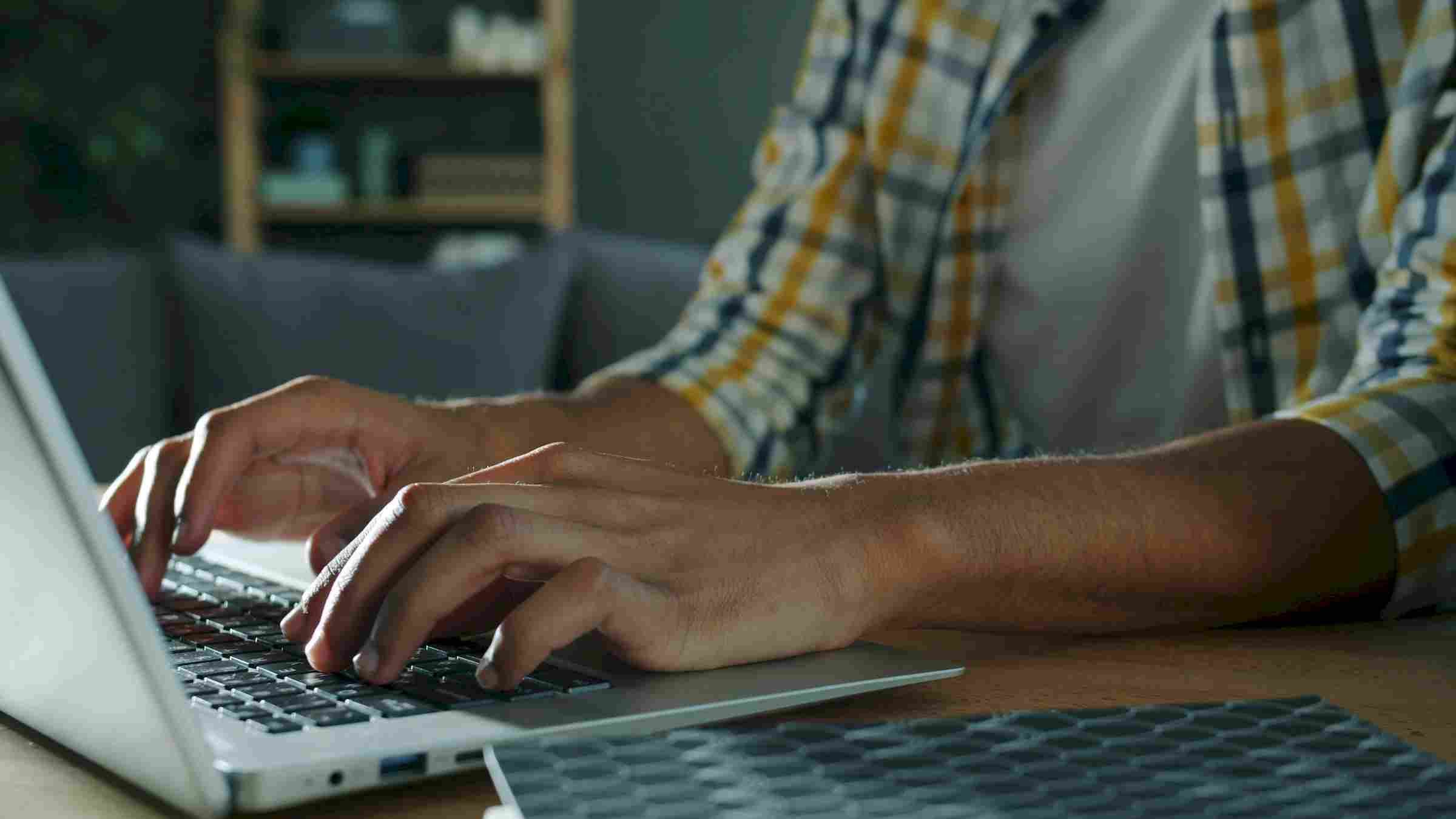 Sierra on 66 Close-up of a person typing on a laptop keyboard at a desk, wearing a plaid shirt.