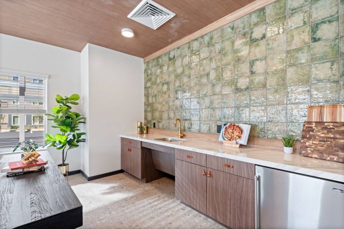 Sierra on 66 Modern kitchen with green tiled backsplash, wood cabinets, gold faucet, and potted plants on counters.