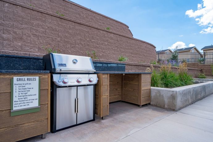 Sierra on 66 Outdoor stainless steel grill with wooden cabinets, stone counter, and posted grill rules near a retaining wall.