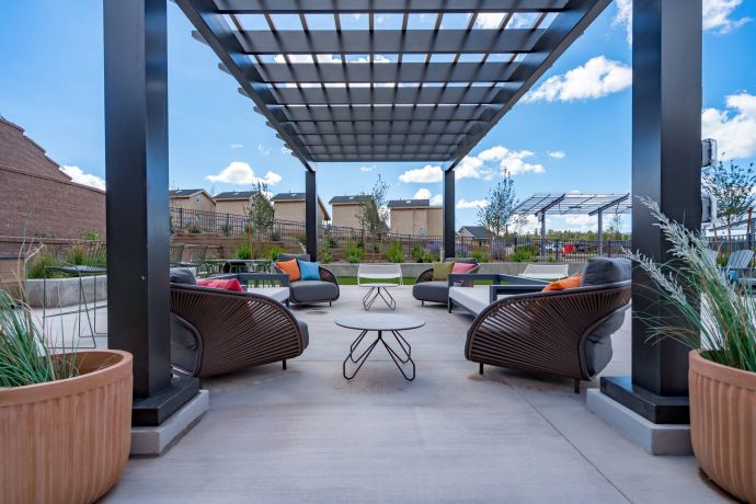 Sierra on 66 Modern outdoor patio with cushioned seating under a pergola, surrounded by plants and clear blue sky.