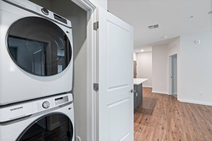 Sierra on 66 Stacked washer and dryer in a laundry closet next to an open door leading to a modern kitchen and living area.