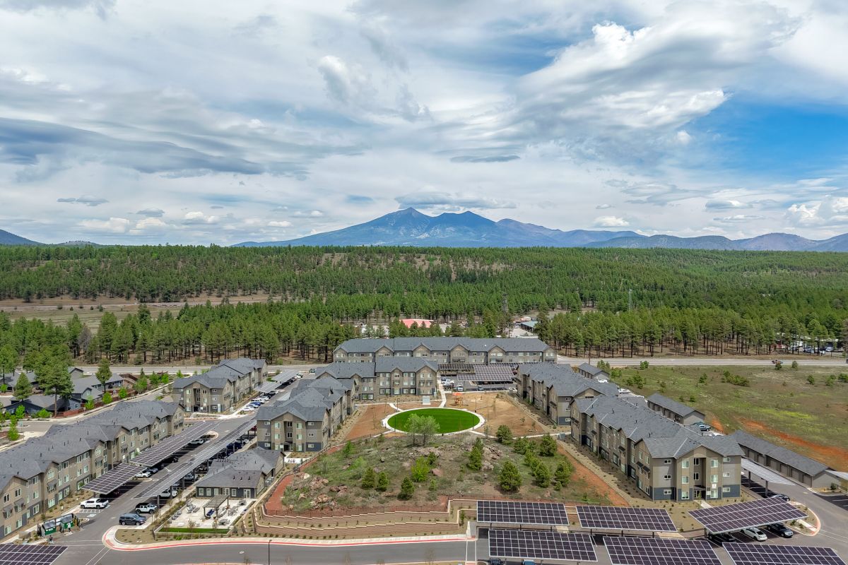 Sierra on 66 Aerial view of apartment buildings surrounded by trees with mountains and a cloudy sky in the background.
