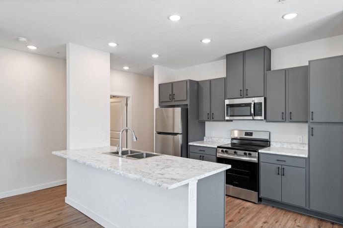 Sierra on 66 Modern kitchen with gray cabinets, stainless steel appliances, and a marble countertop island with a sink.