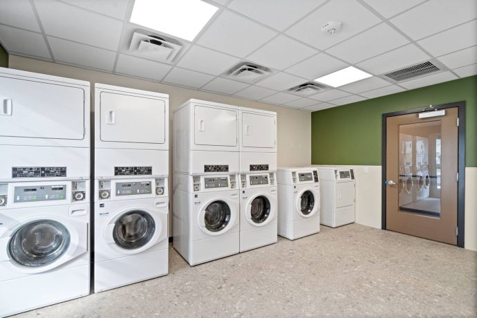 Sierra on 66 A clean laundry room with six white washing machines and dryers, beige walls, and a green accent wall.