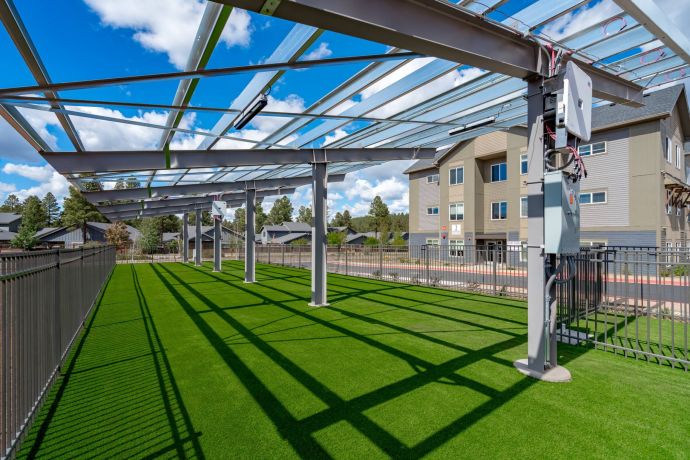 Sierra on 66 Partial glass roof over artificial grass area, with metal beams casting shadows, near residential buildings.