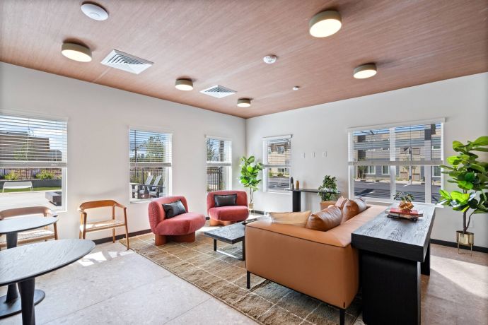 Sierra on 66 Modern lounge with tan sofa, pink chairs, indoor plants, and large windows letting in natural light.