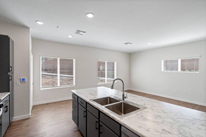 Sierra on 66 Modern kitchen with marble island, double sink, dark cabinets, and large windows letting in natural light.